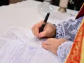 Dłoń w sutannie z koronkowymi mankietami podpisuje akt chrztu do ślubu.