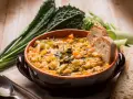 Una ciotola di ribollita fumante, ricca di verdure e fagioli, accompagnata da fette di pane tostato e cavolo nero.