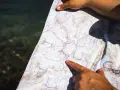 Une main pointe un itinéraire sur une carte topo détaillée, près d'une étendue d'eau.