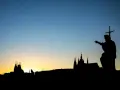 Silhouette d'une statue de saint pointant vers un paysage urbain au coucher du soleil. Le ciel bleu dégradé est le centre d'intérêt de l'image.