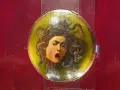 Przerażająca Meduza Caravaggia na okrągłej tarczy, z wężami zamiast włosów i wykrzywioną w krzyku twarzą.