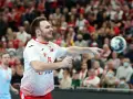 Piłkarz ręczny Polski w akcji, rzuca piłkę. W tle widać trybuny z kibicami, którzy dopingują swoją drużynę w meczu przeciwko Iranowi.