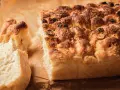 Chrupiąca, złocista włoska focaccia z oliwkami i ziołami, z apetycznie odłamanym kawałkiem.