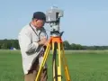 Geodeta precyzyjnie wyznacza granice działki za pomocą tachimetru na statywie, pracując na zielonym polu.