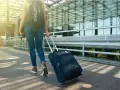 Kobieta z plecakiem Oakley ciągnie walizkę, zastanawiając się, ile może ważyć bagaż podręczny.