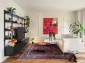 Un galgo se posa sobre un sofá blanco, rodeado de arte abstracto y un tapete persa. El **ruido visual** de los objetos decorativos y la pintura vibrante crea un ambiente ecléctico.