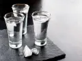 Drei Gläser Wodka mit Eiswürfeln auf dunklem Stein. Wodka wird aus Getreide oder Kartoffeln hergestellt.