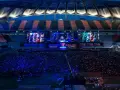 Wielki stadion wypełniony fanami oglądającymi transmisję z gry League of Legends. Na ekranach widać postacie i graczy, a tłum reaguje na emocjonujące rangi w lolu.