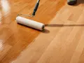 Rullo applica vernice su parquet in corso di levigatura fai da te. Il legno riacquista lucentezza.
