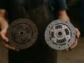 Un meccanico mostra un disco frizione usurato e uno nuovo. I sintomi di una frizione bruciata includono slittamento e odore acre.
