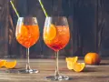 Dwa orzeźwiające drinki z sokiem pomarańczowym, lodem i plasterkiem pomarańczy, ozdobione słomkami.