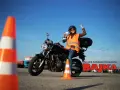 Szczęśliwa kursantka z prawem jazdy kat. A na motocyklu, w kamizelce odblaskowej, na placu manewrowym.