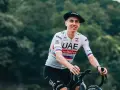 Tadej Pogačar, known for his incredible VO2 max, smiles while riding his bike in a UAE Emirates jersey and a Basque beret.