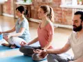 Menschen in einem Yogastudio praktizieren Stress-Meditation, sitzen im Lotussitz auf Matten und schließen die Augen.