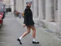 Dziewczyna w stylu Marry Jane, w szarej beretce i krótkiej spódniczce, idzie ulicą.
