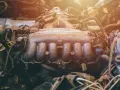Widok na silnik samochodowy z widocznym kolektorem dolotowym. Widać przewody, rurki i inne elementy mechaniczne.