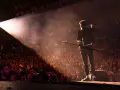 Ein Gitarrist steht im Scheinwerferlicht auf einer Bühne vor einem jubelnden Publikum. Ein Moment, der die Magie der Musikindustrie einfängt.