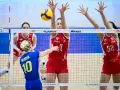 Piłka leci nad siatką podczas meczu liga światowa w piłce siatkowej. Zawodniczki w czerwonych strojach próbują ją zablokować.