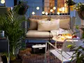 Przytulny mały balkon w bloku, z wygodną kanapą, stolikiem z przekąskami i świecami, ozdobiony lampkami i roślinami.