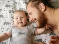 Ein lächelnder Vater und sein Baby liegen auf einer Decke mit Bärenmuster. Die Frage, ob Autismus vererbbar ist, beschäftigt viele, und die Bindung zwischen Vater und Kind ist ein wichtiger Aspekt.