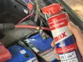 A hand holds a can of INOX MX3 lubricant near a car battery. Does cleaning battery terminals help? This spray might be the answer.