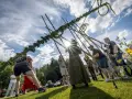 Midsommarstången reses av en grupp människor, en traditionell del av hur firar man midsommar. Solen skiner genom molnen.