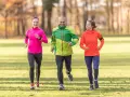 Un gruppo di amici sorridenti segue un programma allenamento corsa e camminata in un parco autunnale.