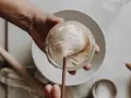 Eine Hand hält ein Glas mit lebendigem Sauerteig, bereit zum Auffrischen. Blasen und Luftlöcher zeigen seine Aktivität.
