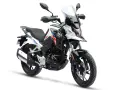 Nowy motocykl gotowy do docierania. Biało-czarny z czerwono-niebieskimi akcentami, z wysoką szybą i terenowymi oponami.