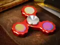 Röd fidget spinner med regnbågseffekter på de tre yttre delarna.
