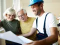 Pareja mayor sonríe mientras revisa planos con un constructor. Posibles bonificaciones mayores 65 años para su proyecto.