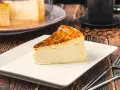 Rebanada de tarta italiana mascarpone con corteza dorada, servida en plato blanco con cubiertos.