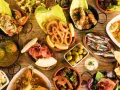 Tapas selber machen: Eine Auswahl an köstlichen spanischen Kleinigkeiten wie frittierte Tintenfischringe, Sardinen, Oliven und Schinken auf einem Holztisch.