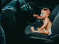 Maluch w pieluszce siedzi za kierownicą, jakby zastanawiał się, od kiedy dziecko może jeździć z przodu.