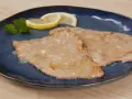 Due scaloppine al limone cremose, guarnite con prezzemolo e spicchi di limone, su un piatto blu.