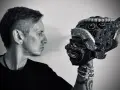 Mężczyzna w czarnym t-shircie patrzy na tradycyjną maskę. Czerń koloru podkreśla tajemniczość sceny.