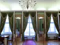 Wnętrze pałacu królewskiego we Wrocławiu. Eleganckie zielone zasłony, złote lustra i kryształowy żyrandol tworzą atmosferę dawnej świetności.