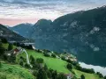 Grönskande bergssluttningar med hus vid en fjord i Norge. Perfekt för att planera dina inreseregler Norge.