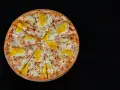 Pizza hawajska z kurczakiem i ananasem na czarnym tle.