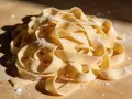Świeży, domowy makaron tagliatelle, gotowy do zupy z makaronem. Złociste wstążki mączne, lekko oprószone mąką, ułożone na drewnianej desce.