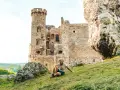 Kobieta odpoczywa na trawie przed ruinami zamku na Szlaku Orlich Gniazd. Ile zamków czeka na odkrycie?