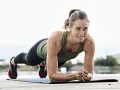 En kvinna i planka på en yogamatta utomhus. Hon tränar sin bålmuskulatur, som om hon gjorde cable crunches.