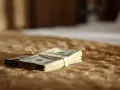 Stos banknotów dolarowych związany złotą wstążką, leżący na brązowym, futrzanym tle.