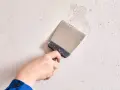 Mano con espátula metálica alisando una pared de yeso con textura irregular.