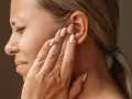 Une femme se tient l'oreille, le visage crispé, comme si elle entendait un bruit sourd dans les oreilles.