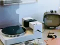 Moderner Plattenspieler mit Vinyl-Schallplatte, Kassetten und Retro-Fernseher. Hier wird die Frage "was ist Vinyl Musik" visuell beantwortet.