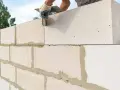 Budowanie ściany z bloczków betonowych. Ręka w rękawicy nakłada zaprawę na kolejny element.