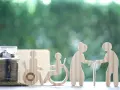 Skarbonka i drewniane figurki symbolizujące osoby w różnym wieku i z niepełnosprawnością. Czy świadczenie wspierające wlicza się do dochodu?
