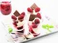 Drei Gläser mit cremigem Dessert, Himbeeren und Schokolade. Ein Glas mit Himbeermarmelade daneben. Schnelles Eis für den Sommer.
