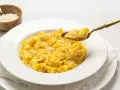 Un cucchiaio d'oro solleva un boccone di cappelletti in brodo fumante da un piatto bianco.